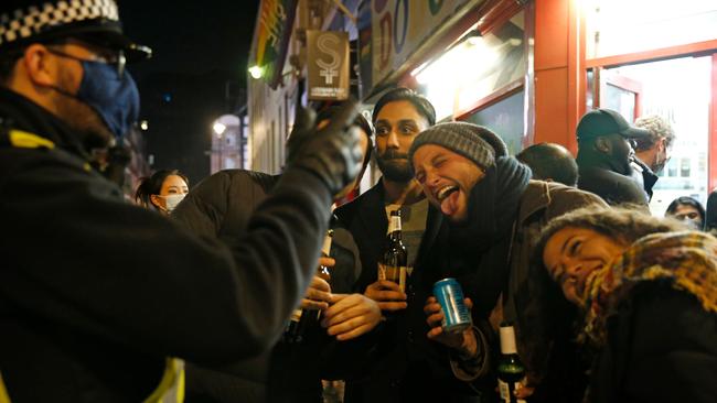 A police officer talks to revellers outside a pub in the soho area of central London. Picture: AFP