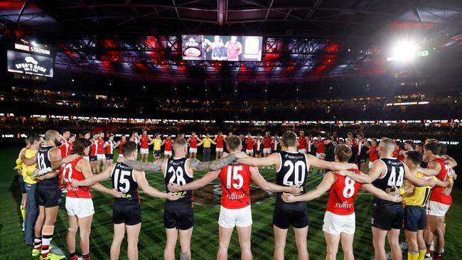 MELBOURNE, AUSTRALIA - JUNE 17: Players, coaches and umpires huddle as Tim Watson and Nathan Burke speak before Spuds Game during the 2022 AFL Round 14 match between the St Kilda Saints and the Essendon Bombers at Marvel Stadium on June 17, 2022 in Melbourne, Australia. (Photo by Michael Willson/AFL Photos via Getty Images)