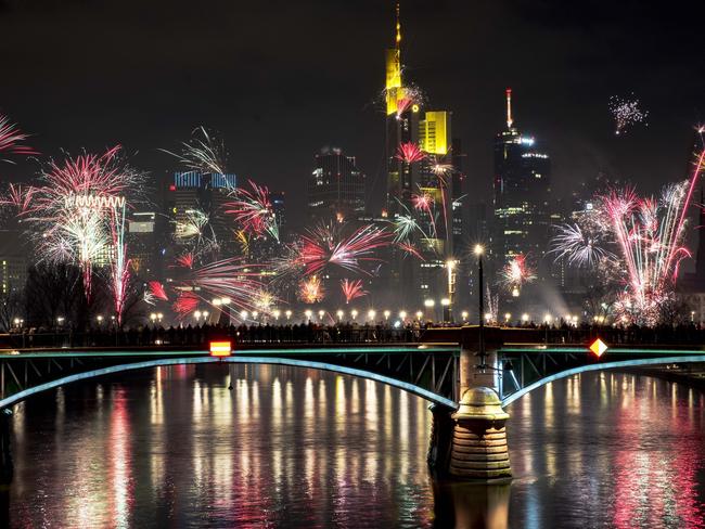 People stand on a bridge and watch fireworks during New Year celebrations near the buildings of the banking district in Frankfurt, Germany. Picture: AP