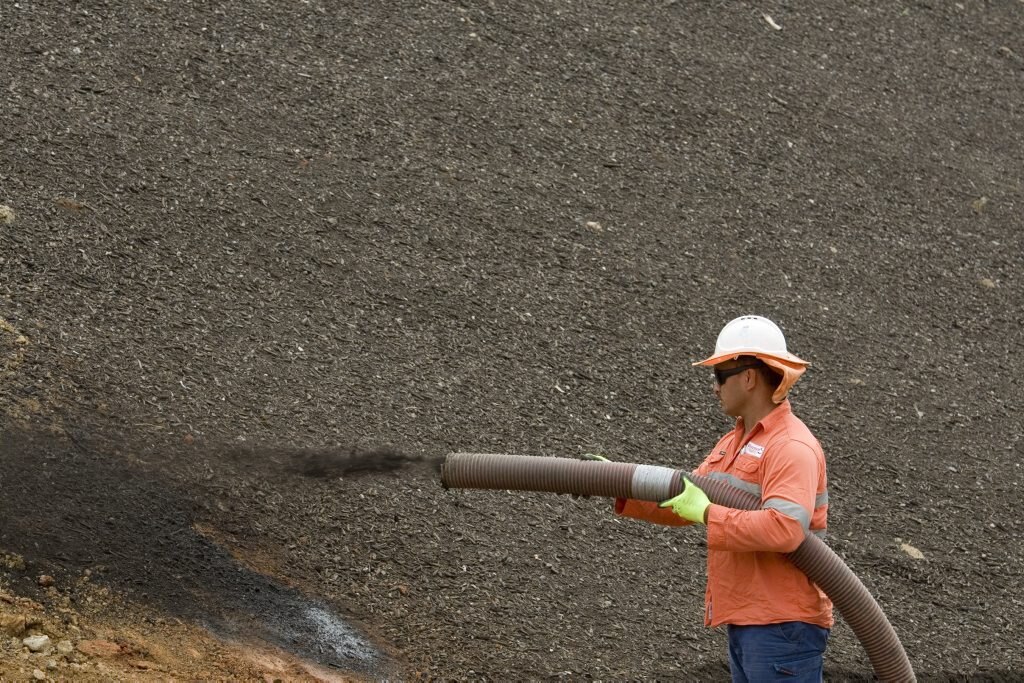 Peni Toia sprays the seed-laced mulch on the roadside. Picture: Kevin Farmer