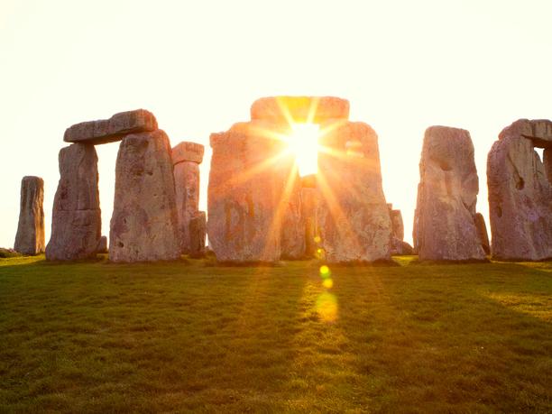 Close-up view of ancient stones during sunset at UNESCO World Heritage Site at Stonehenge, Wiltshire, UK. Sun shines through the stones. Major tourist destination, archeological and pilgrimage site during Summer Solstice and Winter Solstice. Visible grain, softer focus.