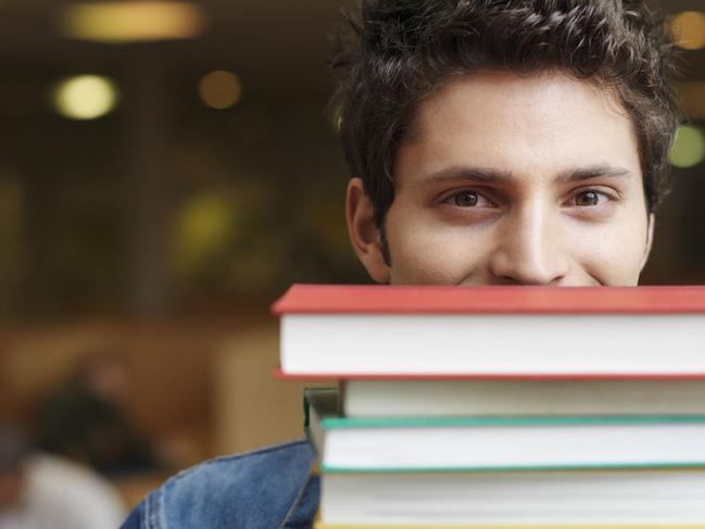 Student holding books in front of face in library, portrait