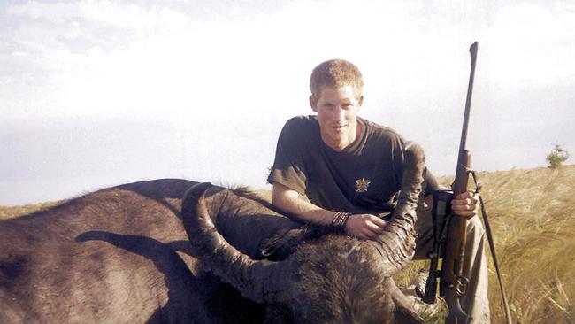 Prince Harry smiles triumphantly and crouches beside the carcass of a recently killed water buffalo.