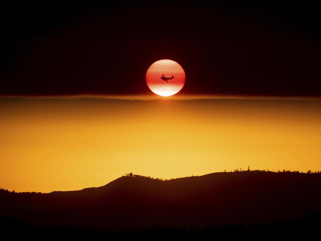 A plane battling the Ferguson Fire passes the setting sun in unincorporated Mariposa County Calif., near Yosemite National Park on Sunday, July 15, 2018. (AP Photo/Noah Berger)