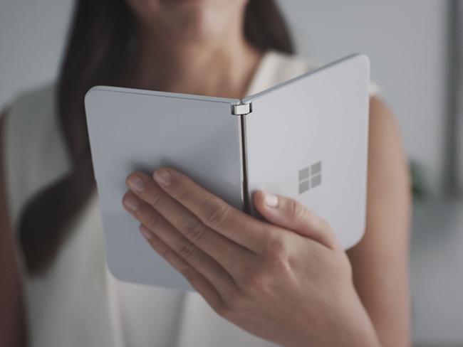 This handout photo obtained October 2, 2019 courtesy of Microsoft shows a woman looking at a new dual-screen device Surface Duo. - Microsoft on October 2, 2019 unveiled Surface tablet computers with twin-screens that opened like books, and a notepad-sized version that put it back in the smartphone game. Surface Duo was touted as the first device in the line-up to fit into a pants pocket, with two 