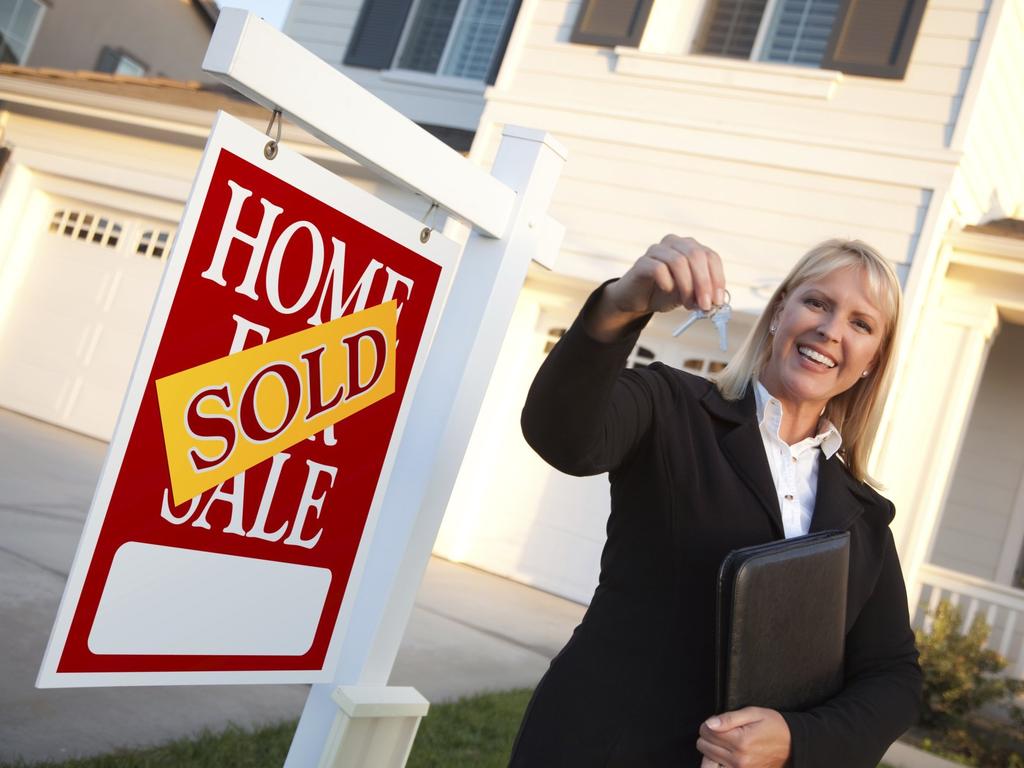 Female Real Estate Agent Handing Over the House Keys in Front of a Beautiful New Home and Real Estate Sign.