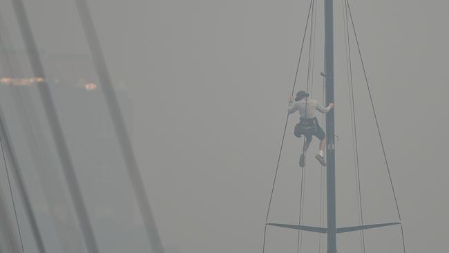 A sailor climbing the mast of a yacht enveloped in haze caused by nearby bushfires at the Cruising Yacht Club of Australia on December 10. Pic: Peter Parks/AFP