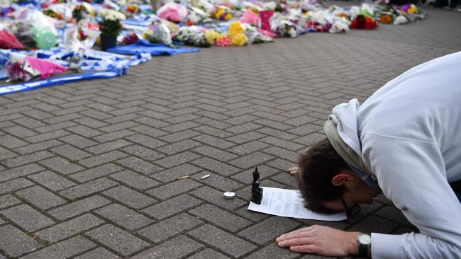 A man kneels with a statue of the Buddha and devotional scripture in front of the floral tributes. Picture: AFP