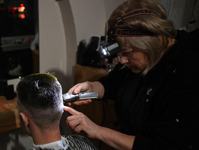 A hairdresser works with a headlamp during a partial blackout in Lviv on November 28, 2024, following Russian strikes on Ukrainian energy infrastructure, amid the Russian invasion of Ukraine. Russia's army on November 28, 2024 launched a massive attack on Ukraine's energy sector, forcing emergency power outages as temperatures dropped to freezing across the country. (Photo by YURIY DYACHYSHYN / AFP)