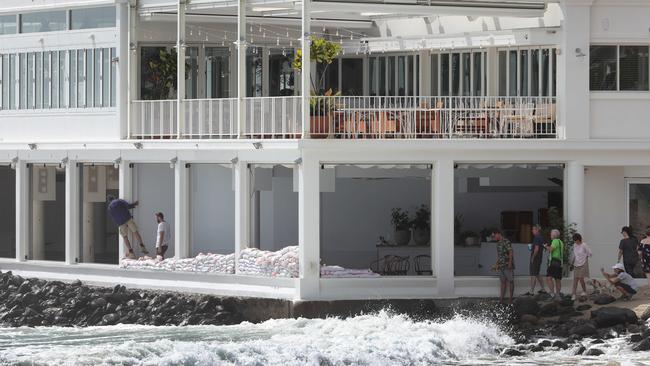 Cyclone Oma is agony for some and ecstasy for others. Staff at Rick Shores at Burleigh Pavilion fight a desperate battle against the king tide and big surf by sandbagging the windows. Picture Glenn Hampson