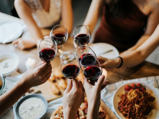 Close up of happy young friends having fun and toasting and celebrating with red wine during party. Photo: iStock