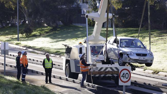 A crane and emergency workers lift a Hyundai sedan wedged on the outbound track. Picture: Emma Brasier