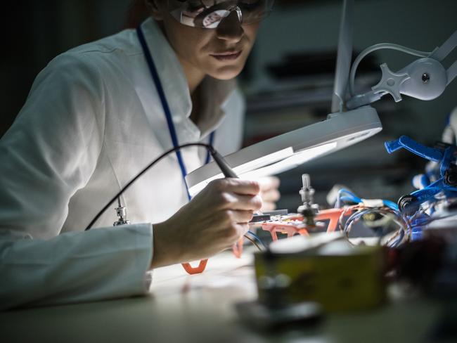 ELECTRONIC/ ENGINEERING CAREERS FOR WOMEN:  Mid adult female electrician working on drone at desk in industry, using magnifying glass;  Robotics generic