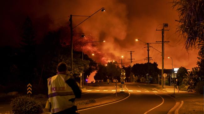 A police officer looks on as the bushfire approaches the Peregian Beach township. Picture: Lachie Millard