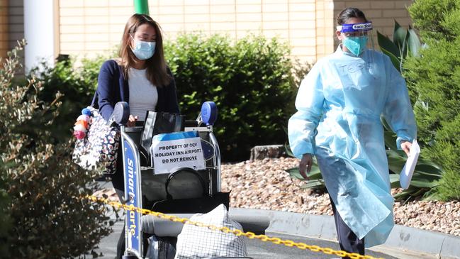 A quarantined traveller is escorted from the Holiday Inn. Picture: David Crosling