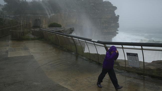 Water rises off the cliffs at Sydney’s Watsons Bay this week as a sightseer struggles in the wind. Picture: Getty Images