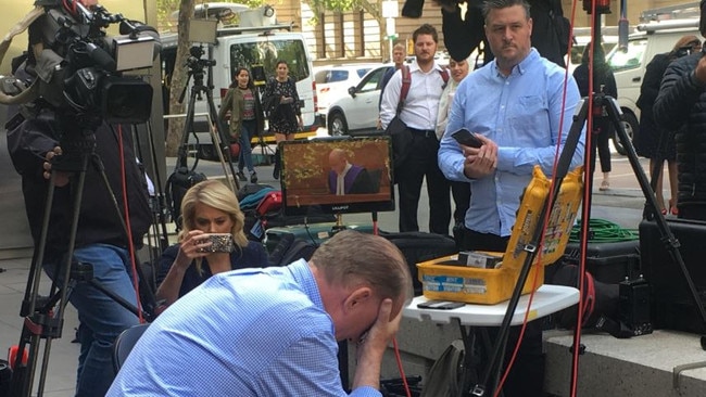 A survivor sits in front of the livestream with his head bowed.