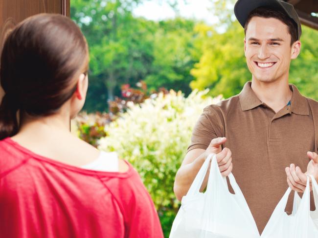 Young delivery man delivering chinese take away food for young woman, standing at the entrance door and holding two plactic bags in hands. Picture: iStock.