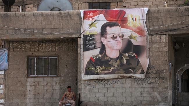  A Syrian soldier sits next to a poster of the Syrian president at the entrance of a refugee camp. Picture: AFP