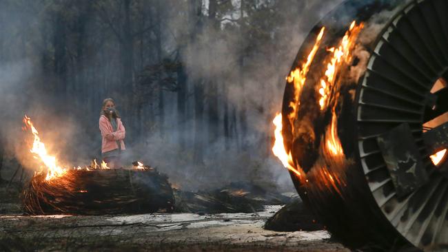 A young girl walks past burning cable spools along a scorched property in Mallacoota. Picture: David Caird