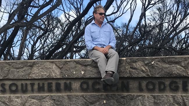 Owner James Baillie on the lodge’s sign amid blackened bush.