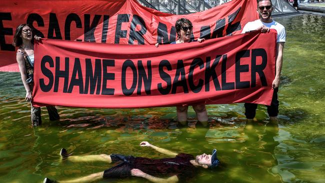 Activists of P.A.I.N. (Prescription Addiction Intervention Now) association - created to respond to the opioid crisis - and of French NGO Aides hold banners reading "Shame on Sackler" and "Take down the Sackler name" in front of the Pyramid of the Louvre in Paris in 2019.