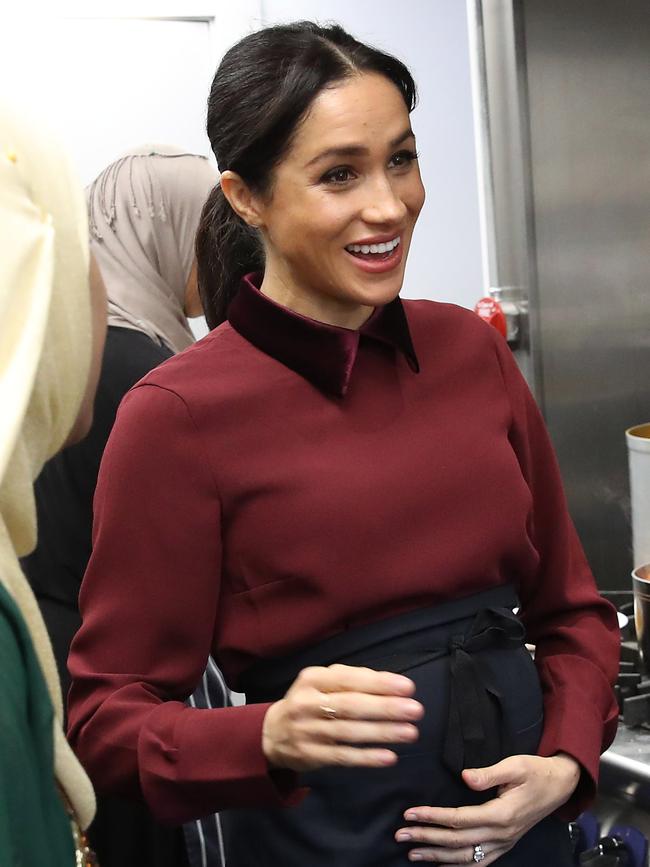 Meghan cradles her bump as she visits the Hubb Community Kitchen. Picture: Getty Images