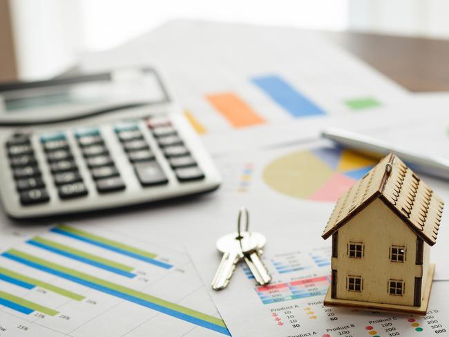 Color image depicting a real estate market and property concept. A wooden model house, a set of house keys, a calculator and pen sit on top of an array of documents with financial bar graphs and pie charts.; property investment generic