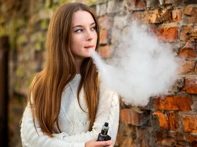 Vaping teenager. Young pretty white caucasian teenage girl with problem skin smoking an electronic cigarette the ruined brick wall on the street in the autumn. Bad habit. Vape activity.