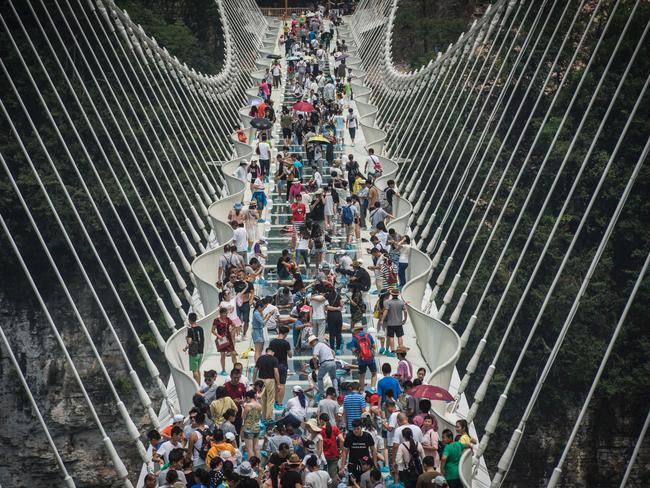 (FILES) This file photo taken on August 21, 2016 shows visitors crossing the world's highest and longest glass-bottomed bridge above a valley in Zhangjiajie in China's Hunan Province on August 21, 2016. The world's longest glass bridge, over a scenic canyon in China, has been closed on September 3, less than two weeks after it opened after being overwhelmed by a swarm of visitors. / AFP PHOTO / FRED DUFOUR