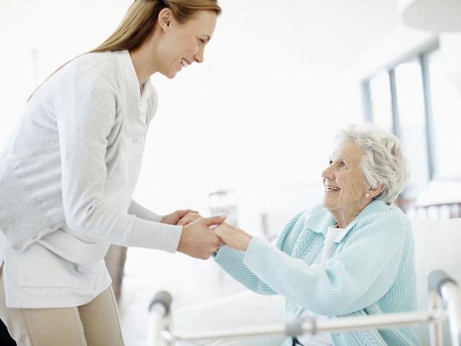 Daughter helps her smiling mother stand up in preparation to use her walker, aged care generic, for moneysaverHQ