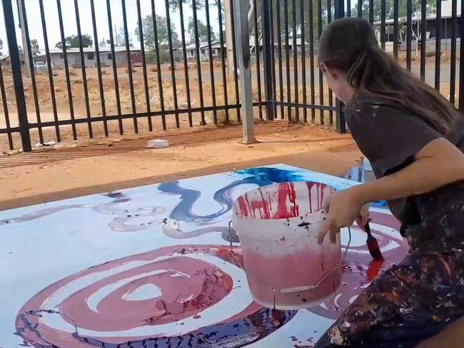 Stills taken from video where a non-indigenous employee is seen contributing to a painting by (Indigenous) artist Yaritji Young. The employee wearing darker clothing and holding a paint brush is Rosie Palmer, manager of Tjala Art in the settlement of Amata in the APY Lands.