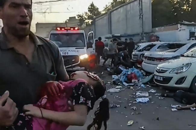 In this image grab taken from an AFPTV video footage shows a man carrying an injured girl near an ambulance damaged in a reported Israeli strike in front of Al-Shifa hospital in Gaza City on November 3, 2023