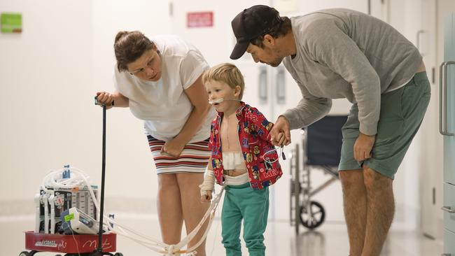 Harry, with mum Simone and father Chris, begins to walk again through the pain of major surgery. The trailer caries fluid drains. Picture: Jason Edwards