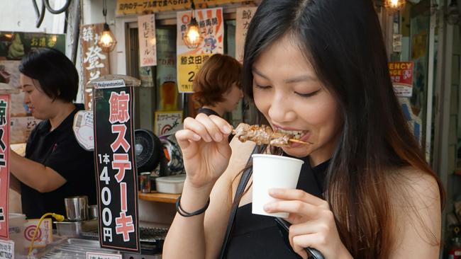 This July 2, 2019 picture shows a woman eating whale meat in front of Tsukiji's whale meat restaurant in Tokyo. - Japan's resumption of commercial whaling has prompted fury from other countries and campaigners, with activists saying that one of the three species targeted is threatened with extinction and sub-populations of the other two are depleted. (Photo by Karyn Nishimura / AFP)