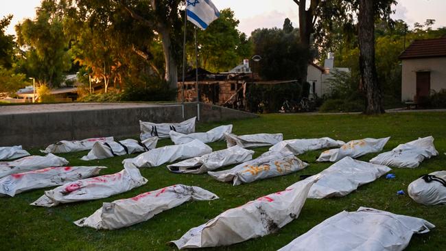 An Israeli flag flies over body bags of over 20 dead Hamas militants with the word "terrorist" written in Hebrew, on a main field at Kibbutz Be'eri, where dozens of civilians were killed days earlier near the border with Gaza.