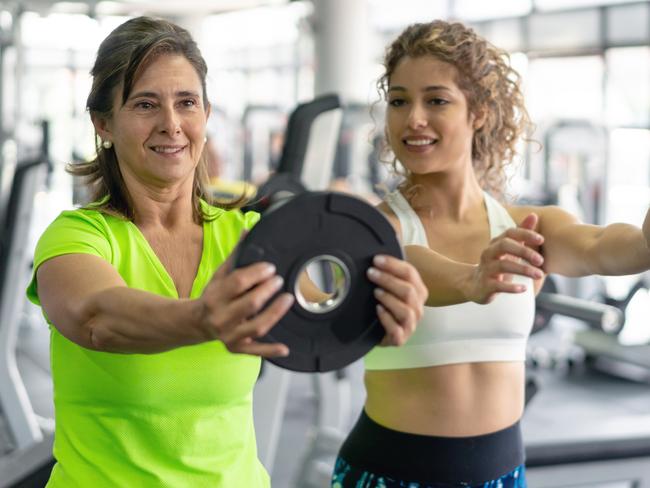 Personal trainer at the gym showing mature woman how to do the exercise both looking focused