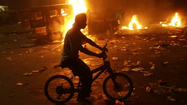 A man rides a bicycle near burning police trucks following a clash outside the presidential palace in Jakarta, Indonesia. Picture: Achmad Ibrahim.