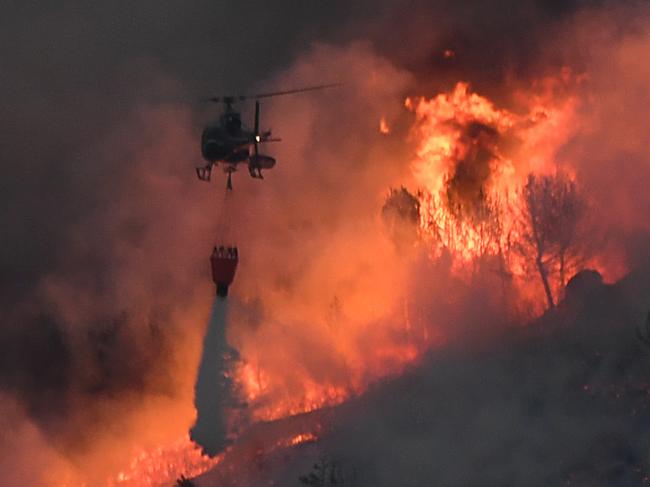 TOPSHOT - An helicopter carries an extinguisher in the struggle against a fire that spread near Vitrolles, southern France on August 10, 2016. France mobilised 1,500 firefighters August 10, 2016 to deal with wildfires in the countryside north of Marseille that have gutted buildings and forced more than 1,000 people to flee their homes. Whipped up by strong winds, the blaze took hold around 3:30 pm (1330 GMT) and has spread over 2,260 hectares (5,600 acres) of scrubland, grass and some wooded areas, according to firefighters. The blaze -- which comes after low rainfall in winter and spring left southeast France extremely dry -- sent a huge pall of smoke into the sky over the port city of Marseille. / AFP PHOTO / BORIS HORVAT