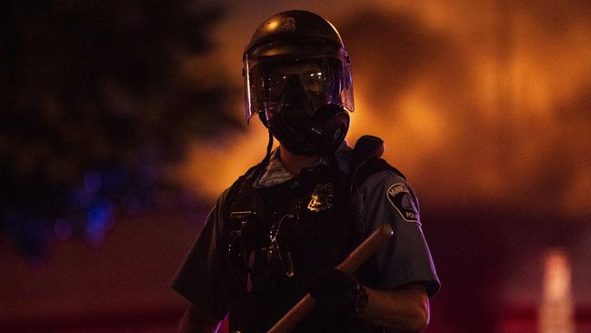 MINNEAPOLIS, MN - MAY 27: A police officer stands with a baton as a fire burns inside of an Auto Zone store near the Third Police Precinct on May 27, 2020 in Minneapolis, Minnesota. Businesses near the Third Police Precinct were looted and damaged today as the area has become the site of an ongoing protest after the police killing of George Floyd. Four Minneapolis police officers have been fired after a video taken by a bystander was posted on social media showing Floyd's neck being pinned to the ground by an officer as he repeatedly said, "I cant breathe". Floyd was later pronounced dead while in police custody after being transported to Hennepin County Medical Center.   Stephen Maturen/Getty Images/AFP == FOR NEWSPAPERS, INTERNET, TELCOS & TELEVISION USE ONLY ==