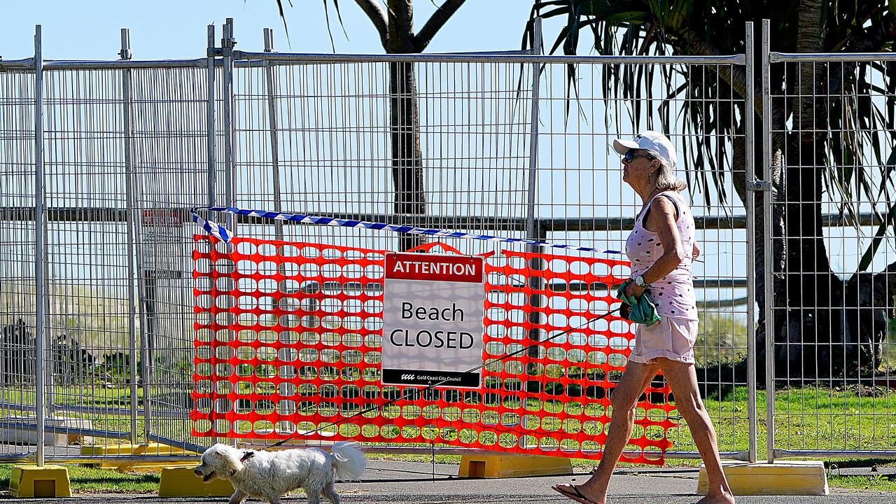 A woman walks her dog past a closed beach at Coolangatta on the Gold Coast. Queensland will be the first state to start relaxing some of its social distancing measures. Picture: AAP / Dave Hunt