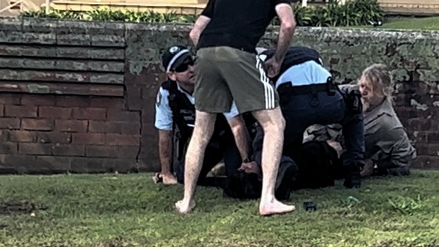 Brendon James Brooks is held with his head on the ground as two residents - one standing up and the second holding Brooks’ legs - assist police. Picture: Supplied.