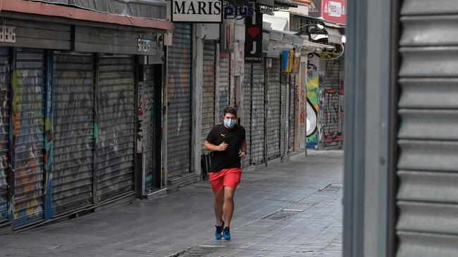 A man jogs by closed businesses in central Athens on the first day of a three-week lockdown. Picture: AFP