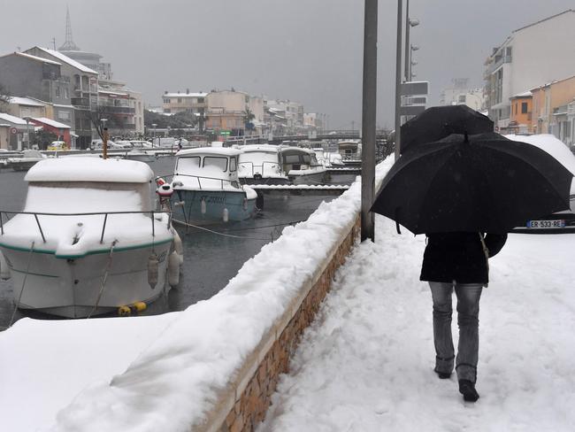 People walk with umbrellas down a snow-covered road near boats docked in Palavas-les-Flots, in the south of France, on February 28, 2018. Europe remained on February 28 gripped by a blast of Siberian weather, accounting for at least 24 deaths and carpeting palm-lined Mediterranean beaches in snow. Picture: AFP