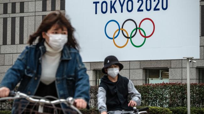 Cuclists in Tokyo ride past a Tokyo Olympics sign. Picture: Getty Images