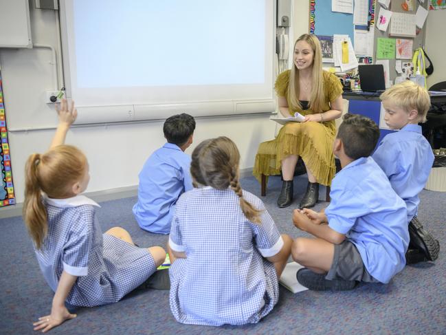 Young woman teaching multi racial students in primary school on the carpet