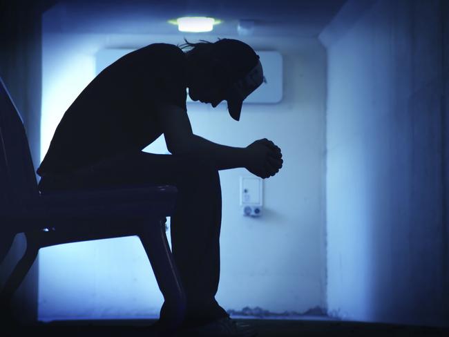 Suicide - Should the children be told? Silhouette of young man sitting with hands clasped together.