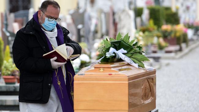 A priest wearing a face mask checks a book of funeral rites as he gives the last blessing to a deceased person outside the cemetery of Bolgare, Lombardy. Picture: AFP