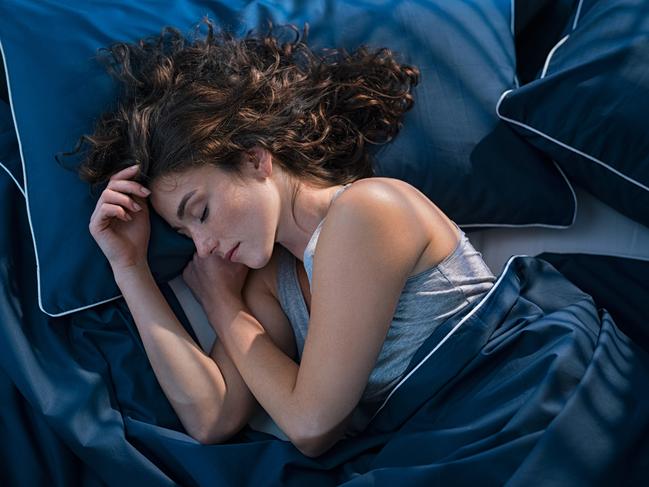 Top view of young woman sleeping on side in her bed at night. Beautiful girl sleeping profoundly and dreaming at home with blue blanket. High angle view of woman asleep with closed eyes. Photo: iStock