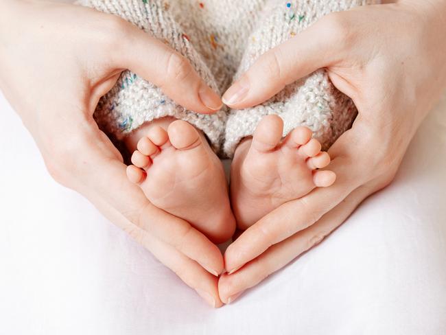 Baby feet in mother hands. Tiny Newborn Baby's feet on female Heart Shaped hands closeup. Mom and her Child. Happy Family concept. Beautiful conceptual image of Maternity